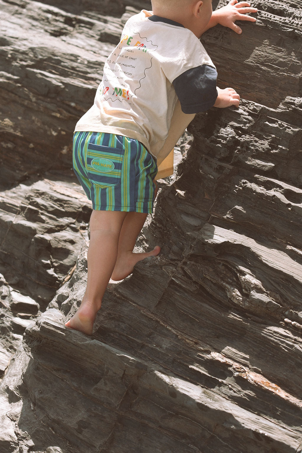 Child wearing blue, green and yellow striped shorts.