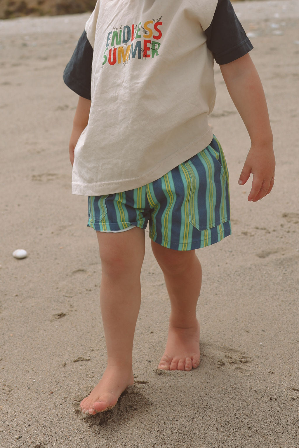Child wearing blue, green and yellow striped shorts.
