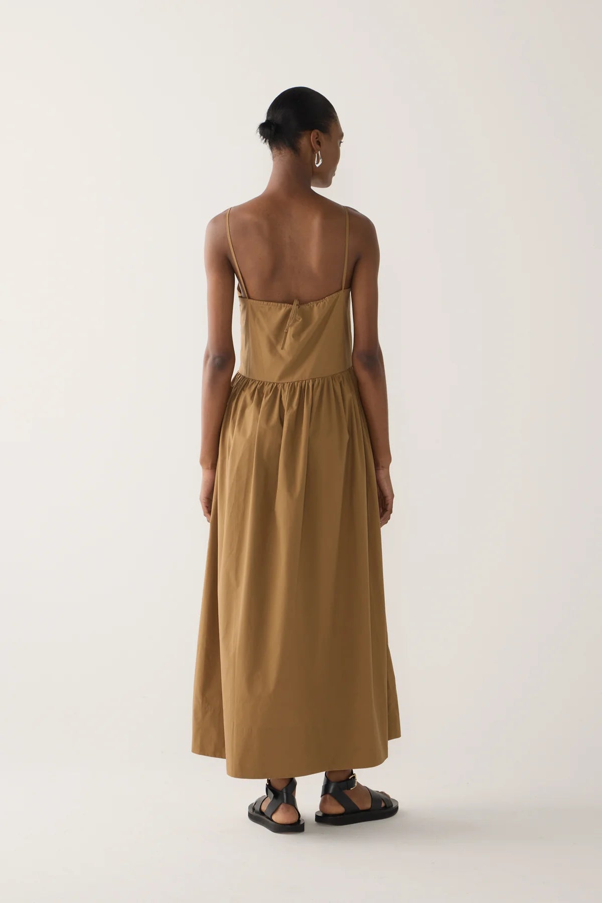 Back view of odel wearing Amanda dress from Foemina. Cocoa cotton tencel spaghetti strap dress with gathering at bodice seam, adjustable straps, side seam pockets and bodice seam details