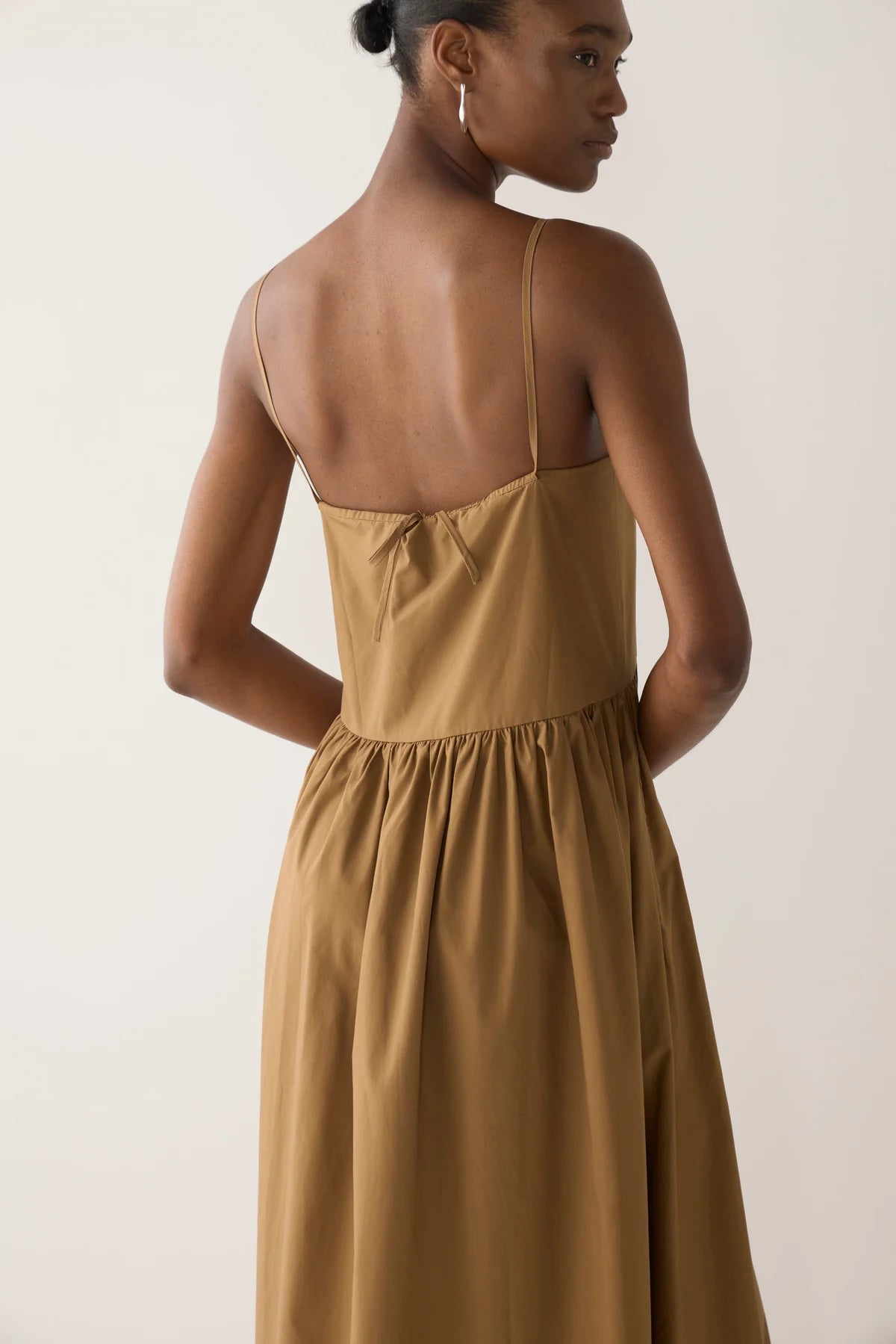 Close up of back view of model wearing Amanda dress from Foemina. Cocoa cotton tencel spaghetti strap dress with gathering at bodice seam, adjustable straps, side seam pockets and bodice seam details