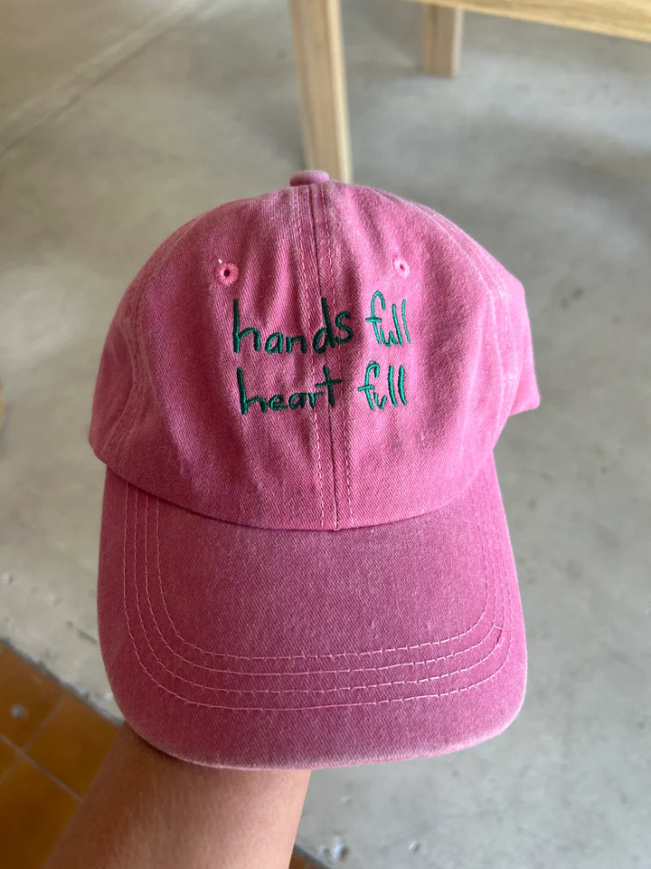 Pink cap with green “hands full, heart full ” text made from cotton