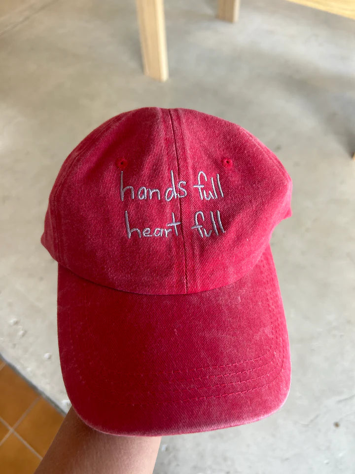 Red cap with blue “hands full, heart full” text made from cotton