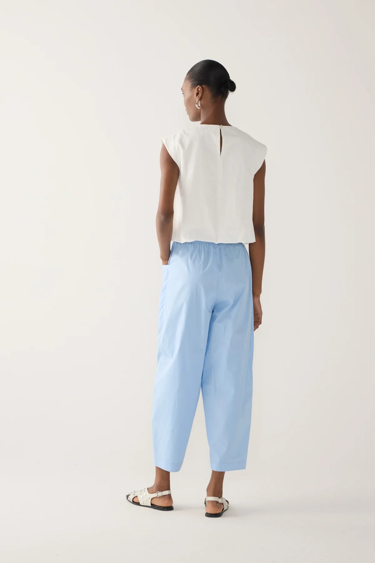 Back view of Model wearing chambray cropped barrel leg organic cotton poplin pants with a drawstring waist and front patch pockets