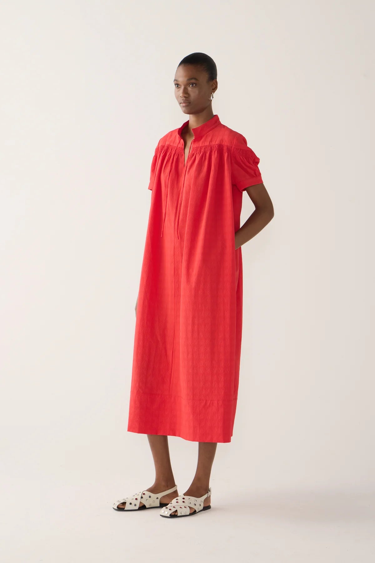Model wearing Kaya Dress from Foemina.  rouge seersucker, with cap sleeve, rusching details across shoulder seam, self tie at front neck, tick hem detail.