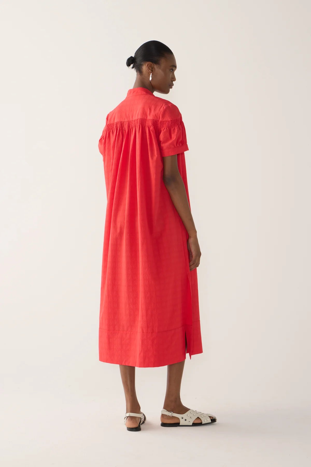 Back view of a model wearing Kaya Dress from Foemina.  rouge seersucker, with cap sleeve, rusching details across shoulder seam, self tie at front neck, tick hem detail.