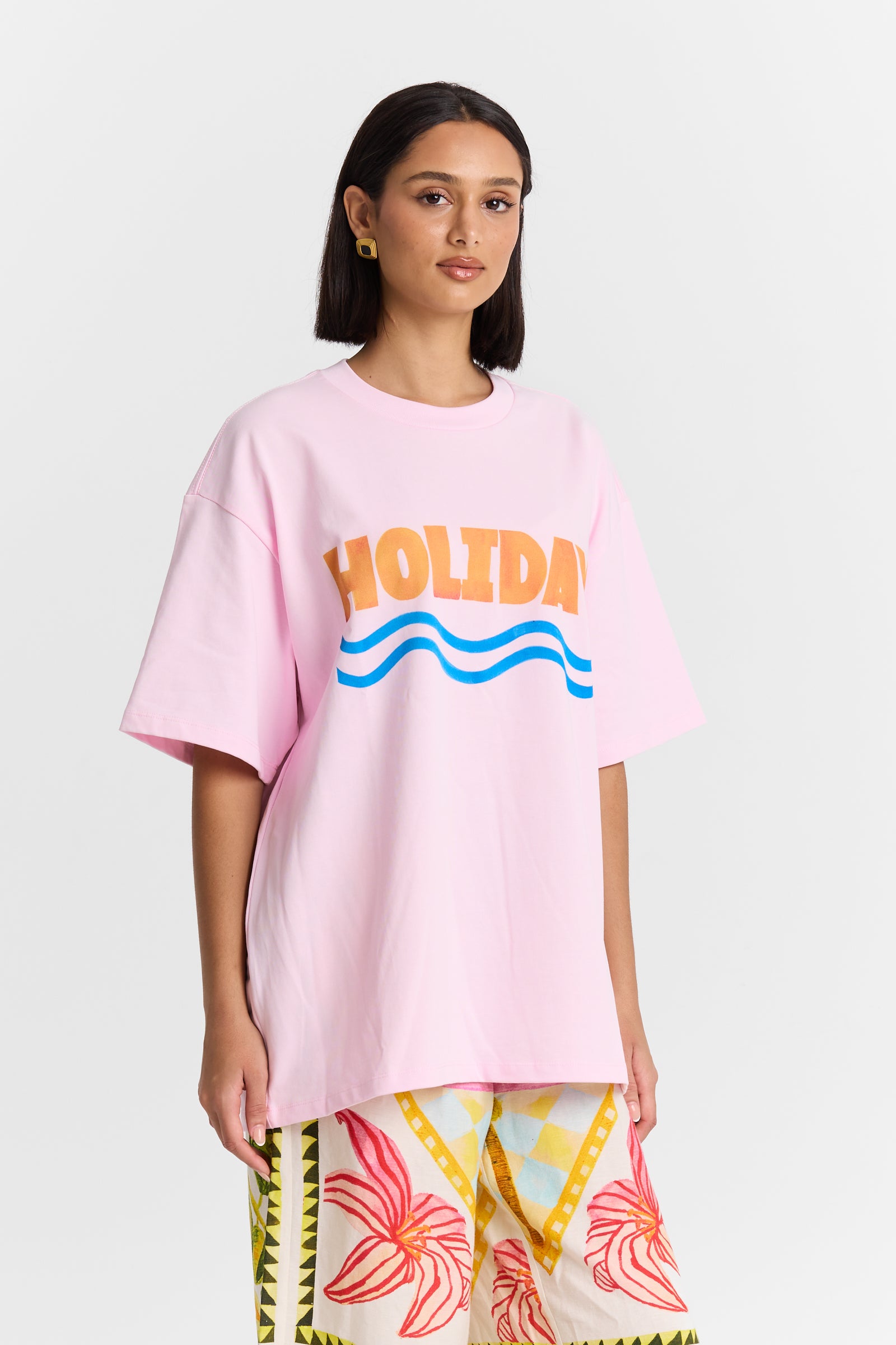 A woman wearing a MAKU pink t-shirt with 'HOLIDAY' and wave graphics on a white background
