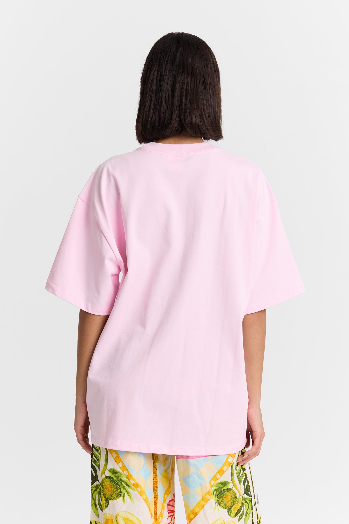 Person wearing a light pink oversized t-shirt with colorful pants on a white background