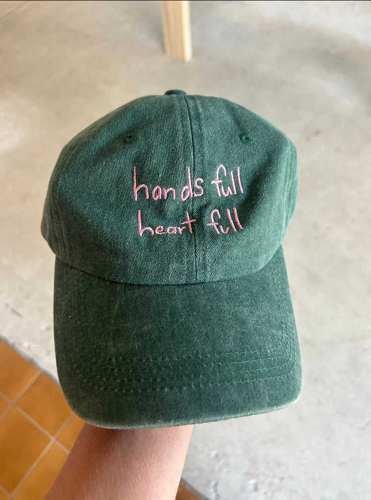 Green cap with pink “hands full heart full” text made from cotton